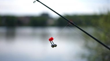 Fishing rod sinker on equipment outdoors at background of river water. Side view fishing tool on summer sunrise on lake shore. Hobbies and relaxation concept