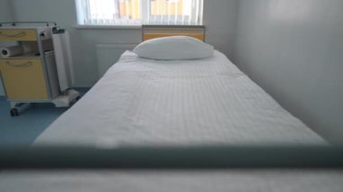 Single bed in modern hospital indoors with sunny window at background. Comfortable cozy furniture in medical clinic with no people. Health care and comfort concept