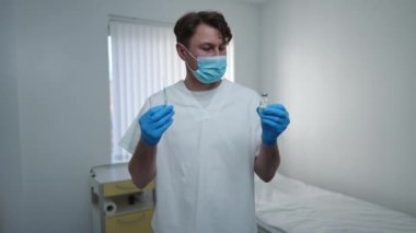 Hastane koğuşunda şırınga ve koronavirüs aşısı ile poz veren maske takmış kendine güvenen bir doktorun portresi. Üniformalı beyaz adam klinikte aşı reklamı yapıyor.