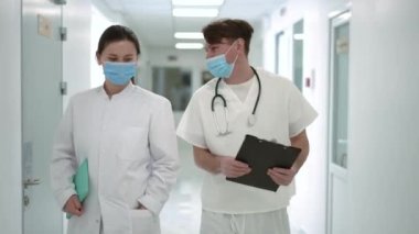Hastane koridorunda yürüyen kendinden emin, pozitif doktorların portresi. Kafkas erkek ve kadının koridorda yürürken teşhisi tartışırkenki görüntüsü.