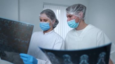 Sorunlu tıbbi üniformalı kadın ve erkek röntgen filmlerini analiz ederek tedavi planlarını konuşuyor. Roentgen 'i incelerken beyin hasarını tartışan profesyonel beyaz doktorların portresi.