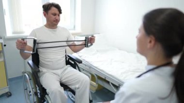 Zayıf motivasyonu olan beyaz bir adam. Önünde bulanık bir doktorla tekerlekli sandalyede oturan direniş bandıyla egzersiz yapıyor. Hastanenin içinde rehabilitasyon gören bir hastanın portresi.