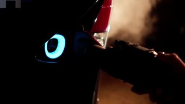 Yakın plan kadın eli arka planda sis olan arabaya elektrik yükleme yapıyor. Karanlıkta elektrikli otomobili şarj eden tanımlanamayan genç, zayıf, beyaz kadın.
