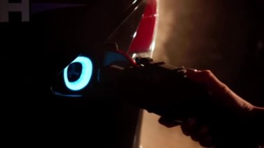 Geceleri dışarıdaki elektrikli otomobil limanına takılı şarj aleti. Arka planda sis görünen modern lüks çevre dostu araca kadın el ekleme cihazı. Otomobil endüstrisi ve