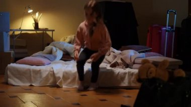 Wide shot scared girl running to mattress in bomb shelter looking away hearing bombardment explosions. Frightened child hiding in war zone in Ukraine during Russian military invasion