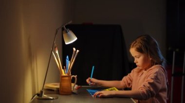 Concentrated Ukrainian girl painting banner as woman entering hugging child smiling. Side view portrait of focused sad daughter hiding with caring mother in bomb shelter indoors drawing