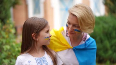 Pretty Ukrainian daughter and beautiful mother looking at each other smiling turning to camera in slow motion. Portrait of confident proud woman and girl with national flag face painting posing