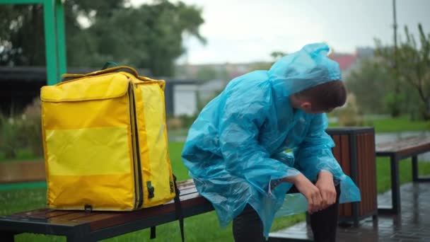 Exhausted Young Courier Sitting Rain Coat Bench City Park Yellow — Vídeo de Stock