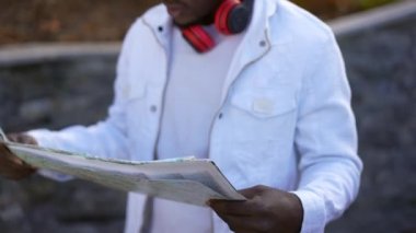 Paper map in hands of troubled man lost in city park. Nervous dissatisfied young unrecognizable African American tourist throwing away map leaving