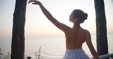 Medium shot of slim elegant ballerina moving hands at background of summer dawn over sea. Live camera follows movement of talented Caucasian woman smiling performing at sunrise. Cinema 4k ProRes HQ
