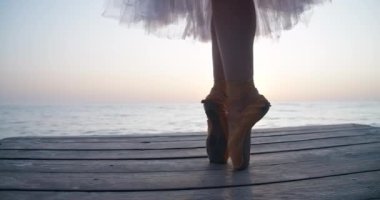 Legs of ballerina in pointies and tutu dancing on tiptoes in sunrays on wooden pier. Unrecognizable talented confident Caucasian woman performing at dawn outdoors. Cinema 4k ProRes HQ