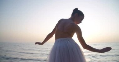 Back view slim woman in tutu dancing in sunbeam in slow motion on sea shore outdoors. Medium shot of graceful elegant ballerina performing in sunrays. Cinema 4k ProRes HQ