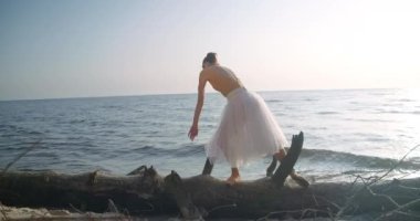 Wide shot graceful woman standing on tree trunk on river bank moving hands in slow motion. Portrait of Caucasian ballerina in sunbeam performing outdoors. Cinema 4k ProRes HQ