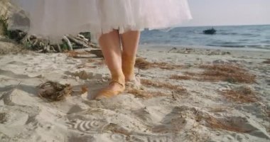 Close-up steps of graceful talented ballet dancer in pointies on yellow sand at background of waves. Unrecognizable Caucasian confident woman walking in slow motion on beach. Cinema 4k ProRes HQ