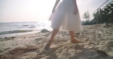 Side view unrecognizable ballerina making steps in slow motion walking in sunbeam on sandy beach. Slim graceful confident Caucasian ballerina strolling outdoors. Cinema 4k ProRes HQ