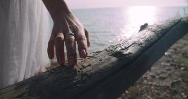 Close-up slim female hand touching wooden fence in slow motion in sunbeam. Unrecognizable young Caucasian woman in tutu outdoors on summer beach at sunset sunrise. Cinema 4k ProRes HQ