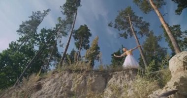 Wide shot bottom view of graceful ballerina dancing doing arabesque in slow motion at background of summer landscape. Caucasian confident beautiful woman performing in sunshine. Cinema 4k ProRes HQ