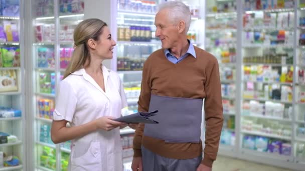 Medium Shot Smiling Woman Pharmacist Senior Caucasian Man Back Bandage — ストック動画