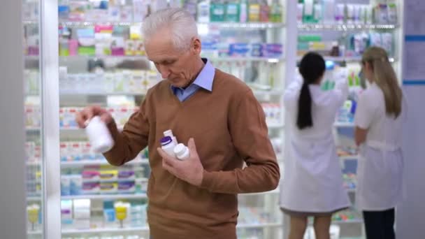 Старший Мужчина Собирает Бутылки Таблетками Полке Аптеке Уходит Размытыми Аптекарями — стоковое видео
