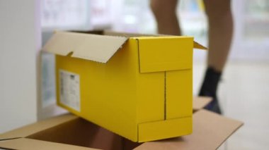 Close-up yellow cardboard box in pharmacy with unrecognizable young woman putting bottles with medications inside. Professional young pharmacist preparing order in drugstore for client