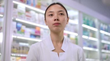 Smart young Asian woman choosing medication on shelf in pharmacy thinking. Portrait of intelligent young pharmacist examining pill bottle making decision. Medicine and hesitation concept