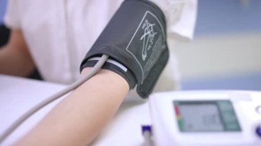 Close-up blood pressure gauge on slim female Caucasian arm. Unrecognizable young woman measuring blood pressure with device sitting indoors. Medicine and health concept