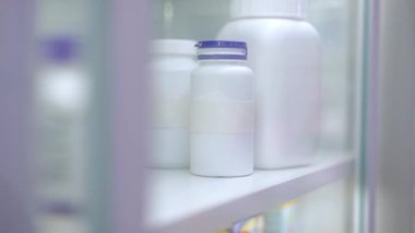 Close-up shelf in pharmacy with female Caucasian hand taking pills leaving closing glass door. Unrecognizable young woman choosing medication buying drugs in drugstore indoors