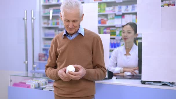 Улыбающийся Пожилой Мужчина Показывает Пальцем Вверх Позируя Таблетками Аптеке Размытой — стоковое видео