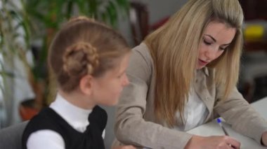Portrait of intelligent beautiful woman talking explaining material to teen student sitting at desk in classroom. Confident positive Caucasian tutor teaching teenage girl. Education and tutoring