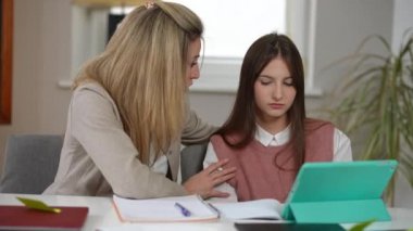 Portrait of Caucasian woman endorsing sad teen girl sitting at desk in classroom. Confident teacher talking to schoolgirl supporting upset student in school. Intelligence and education concept