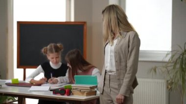 Confident female teacher turning crossing hands looking at camera standing in classroom with teen students. Portrait of gorgeous Caucasian woman posing in school. Confidence and teaching concept