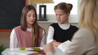 Upset teen schoolgirls sitting at desk in classroom listening to teacher scolding pupils. Portrait of sad Caucasian teenage girls with unhappy facial expressions in school indoors