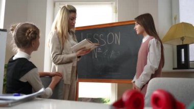 Side view professional teacher and curios student standing at chalkboard in classroom talking. Caucasian woman asking questions as teenage girl thinking on answer. Education and tests concept