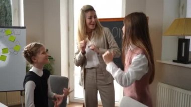 Portrait of happy woman and girls having fun on music lesson in classroom in school. Smiling gorgeous Caucasian woman and pretty cheerful schoolgirls dancing singing enjoying education