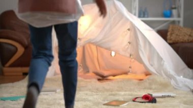 Tent in living room with teen girl entering opening digital tablet scrolling social media. Confident beautiful Caucasian teenager enjoying leisure on weekend at home indoors