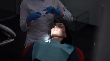 Caucasian woman opening mouth sitting in dental chair with unrecognizable doctor using dental mirror and drill. Portrait of confident patient undergoing treatment in medical clinic. Slow motion