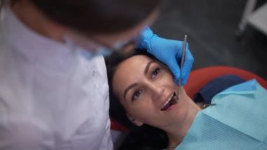 High angle view portrait of Caucasian woman with open mouth in dental chair and doctor using mirror and drill in slow motion. Patient undergoing treatment in clinic as professional dentist treating