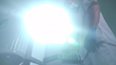 Bottom angle view of dental light shining and young man taking away lamp in slow motion. Patient POV of professional Caucasian doctor adjusting equipment in dentist office in hospital