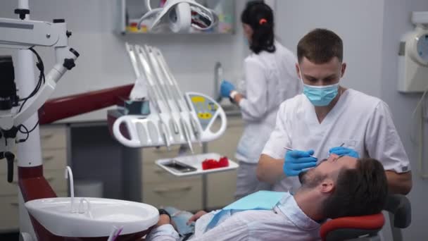Concentrated Dentist Examining Patient Dental Chair Assistant Walking Background Preparing — Stok video