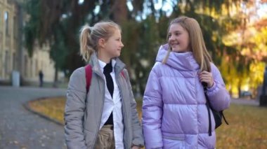 Medium shot of confident intelligent charming classmates gesturing thumbs up looking at camera smiling. Happy Caucasian schoolgirls posing on schoolyard on autumn day. Friendship and education