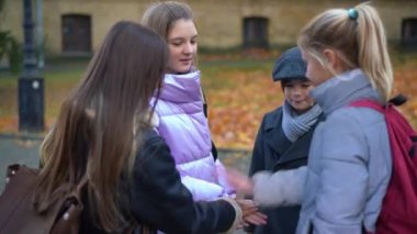 Teenage girls and boy stacking hands smiling standing on autumn schoolyard. Happy confident Caucasian classmates outdoors. education and friendship support