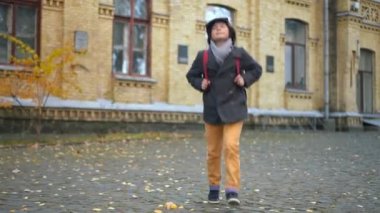 Cheerful excited boy jumping up walking on schoolyard leaving. Portrait of smiling happy Caucasian schoolboy enjoying end of studying on autumn day. Education and happiness concept