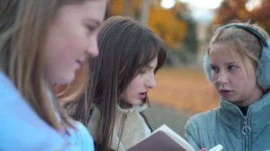 Panning left to right of curios concentrated teen girl discussing homework with classmates outdoors. Charming pretty Caucasian schoolgirl talking with friends studying on schoolyard