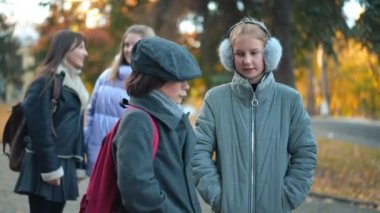 Shy Caucasian boy and girl talking standing on schoolyard with blurred classmates making fun at background. Charming couple with bullies outdoors on autumn day. Relationship and rudeness