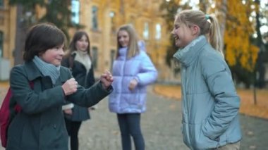 Boy showing fists fighting with girl pushing classmate away laughing. Side view Caucasian schoolmates having fun imitating arguing on college yard