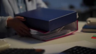 Close-up document folders with unrecognizable blurred young woman taking paperwork leaving in office. Caucasian white collar worker walking away indoors. Business and accounting concept