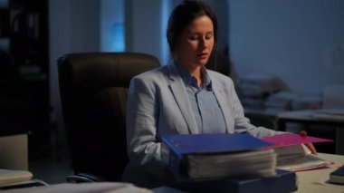 Portrait of dissatisfied tired woman sighing stacking document folders with paperwork looking away. Exhausted overworking Caucasian manager sitting at table in darkness thinking. Disbalance concept