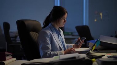 Intelligent beautiful Caucasian woman surfing Internet on laptop picking up phone talking. Side view portrait of concentrated confident female employee working indoors in office in the evening