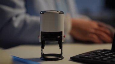 Close-up round seal and calculator on table with hands of blurred woman counting cash money at background. Unrecognizable successful notary businesswoman calculating income in office indoors