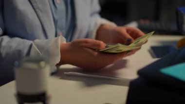 Young unrecognizable Caucasian woman counting money sealing envelope signing with pen. Confident professional accountant calculating cash income sitting in office indoors